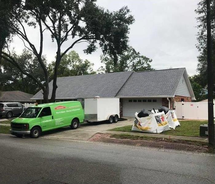 Green van parked in front of a house, two white bags full of trash on sidewalk